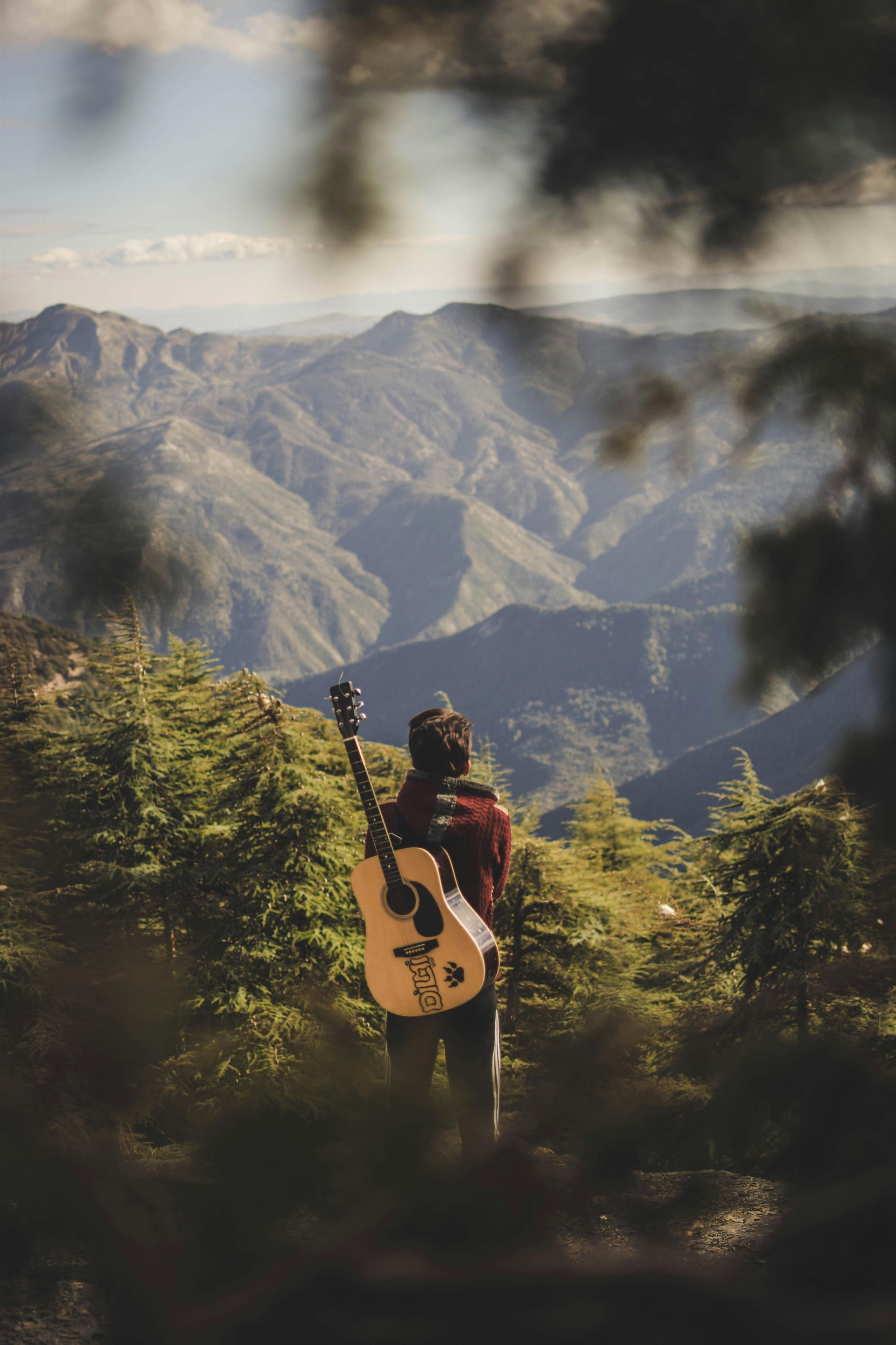 Man with guitar walking hillside with mountains in background