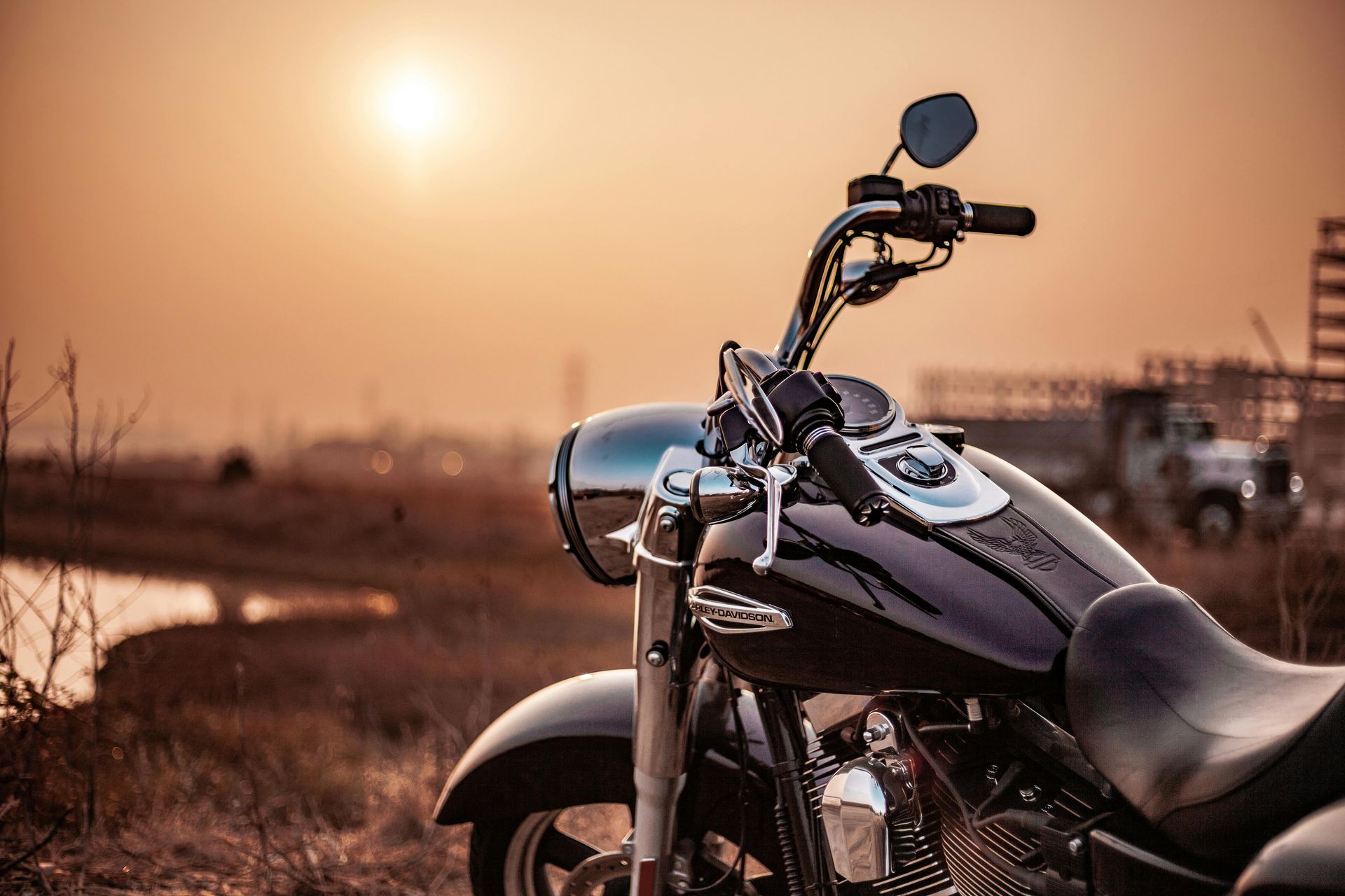 Motorcycle posed on grass field with water and hazy sun in the background