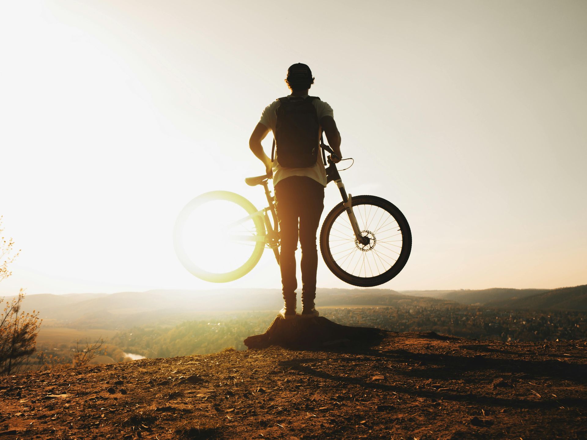 Person holding bike in the air on top of the hill surrounded by bright sunlight
