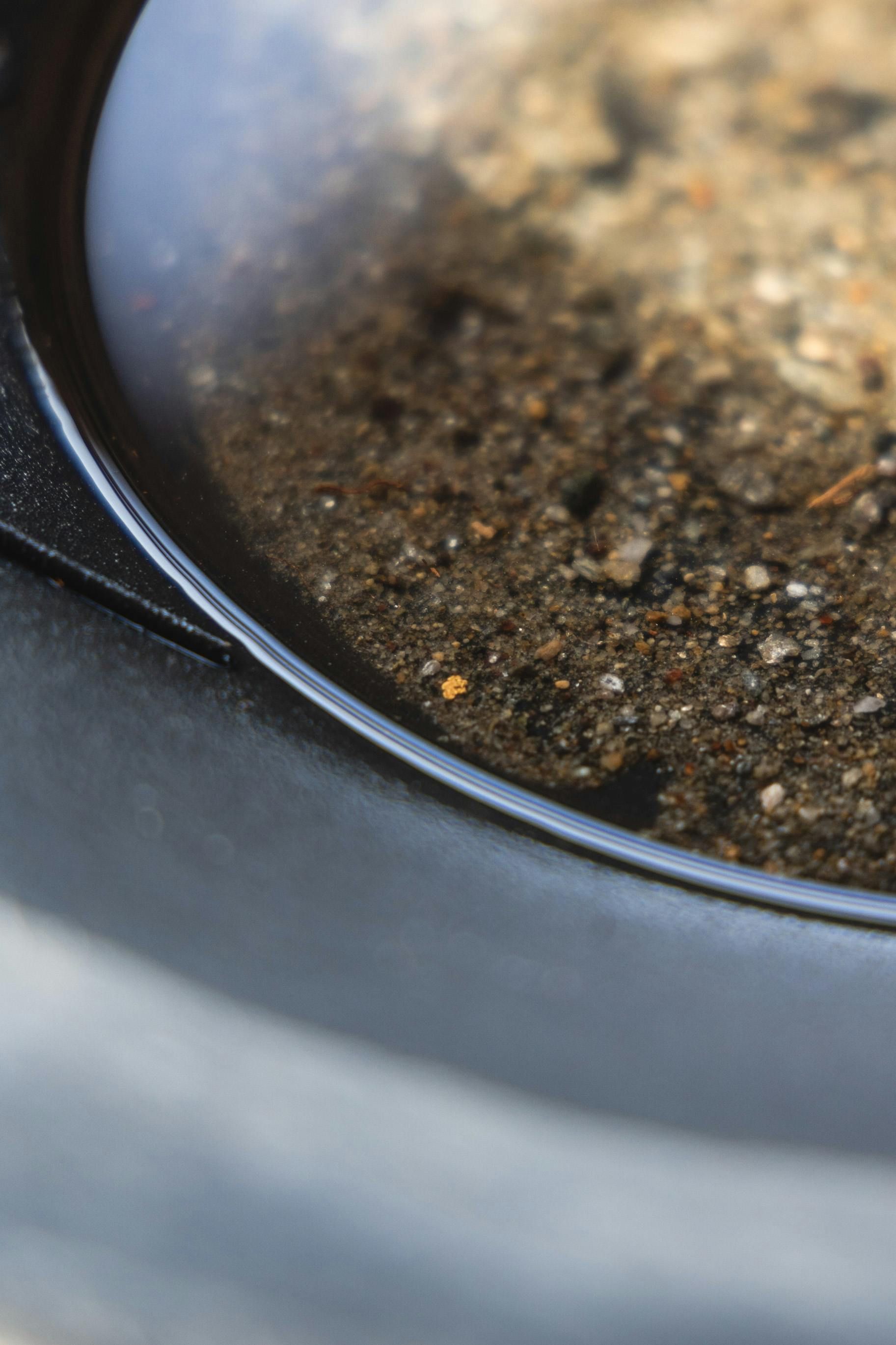 Metal pan with rocks, dirt, water, and gold flakes