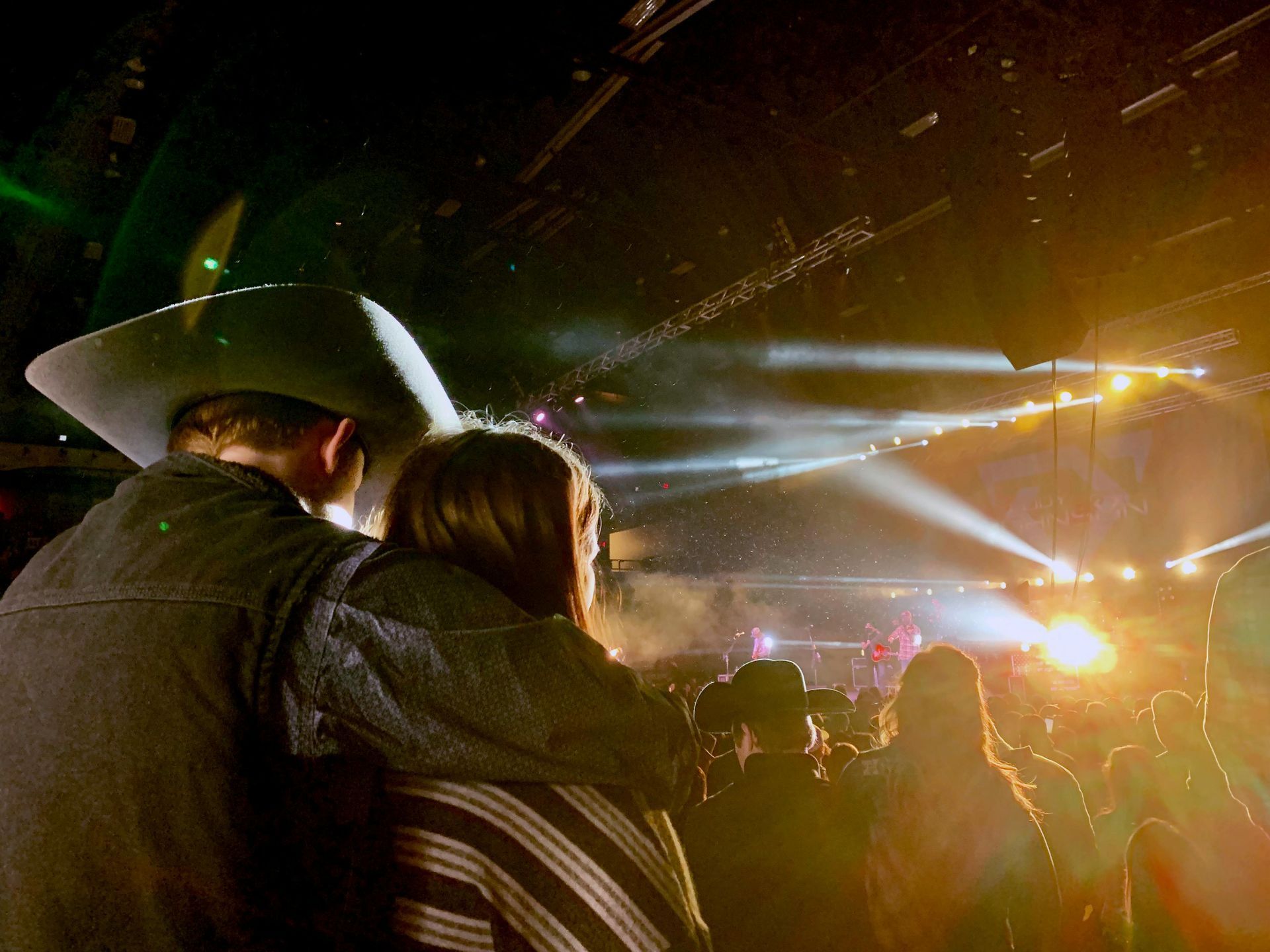 Cowboy with his arm wrapped around his significant other at a live music venue