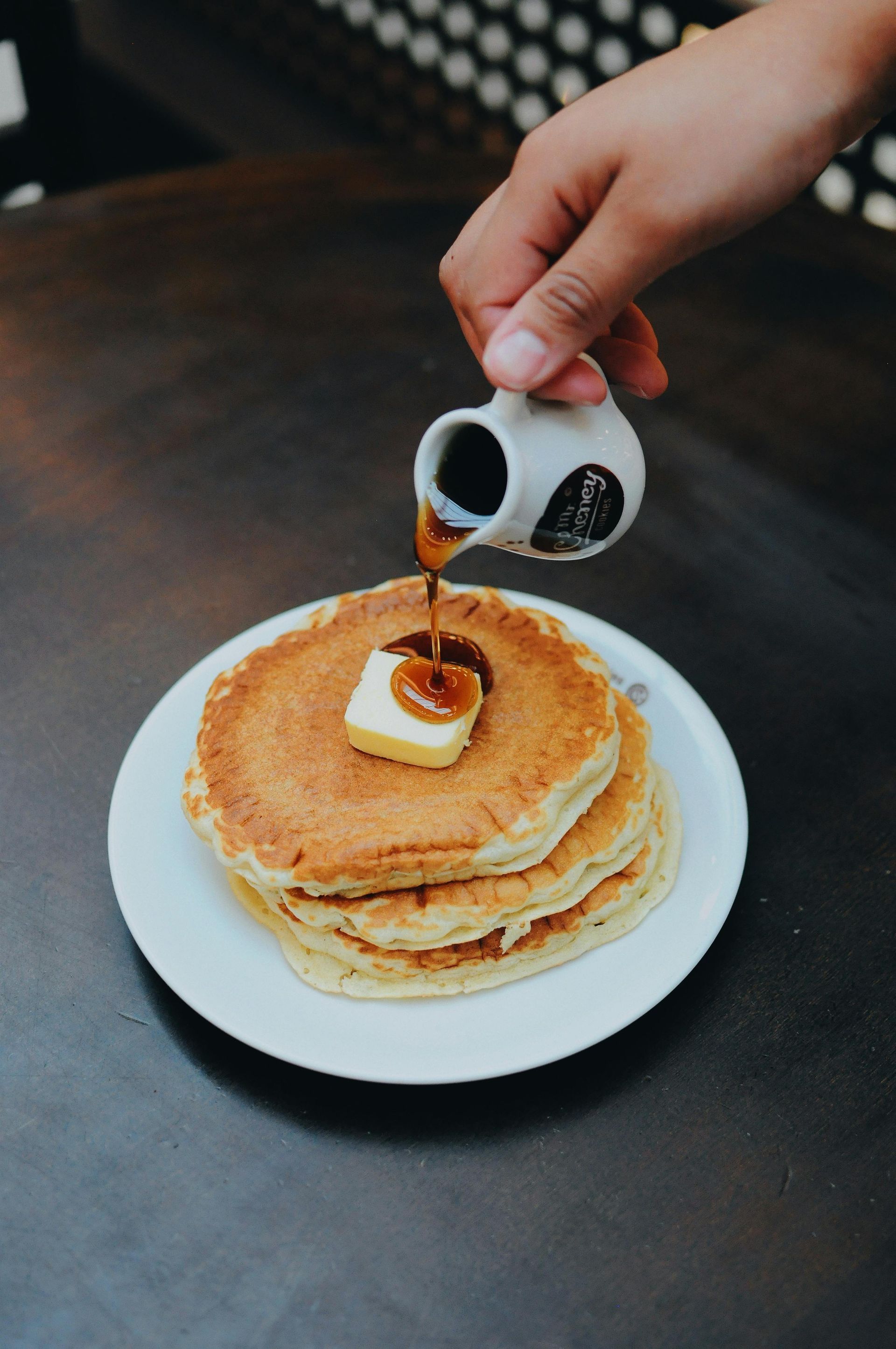Someone pouring syrup over stacked pancakes with butter on top