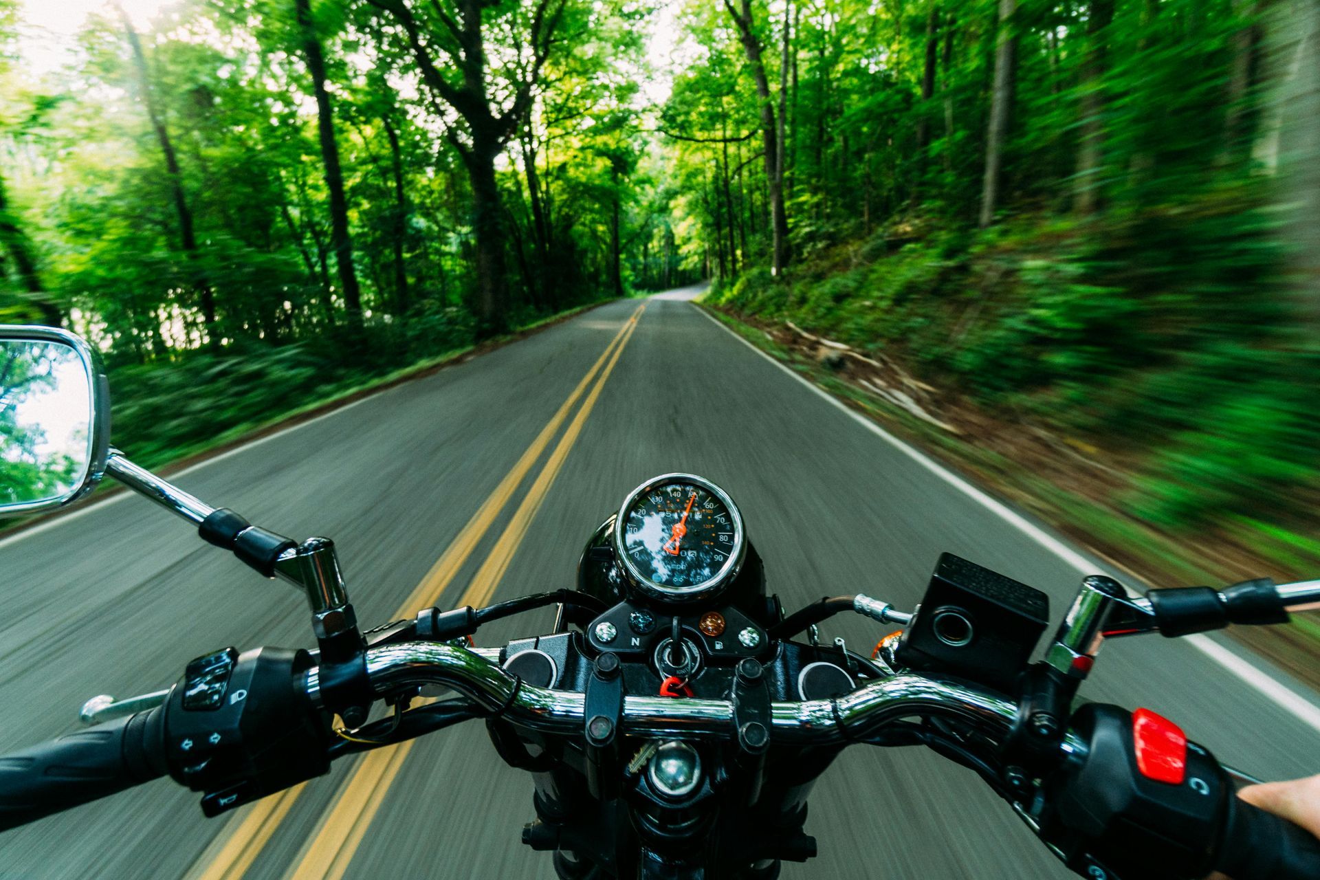 Motorcycle riding quickly down a clear road, surrounded bywilderness