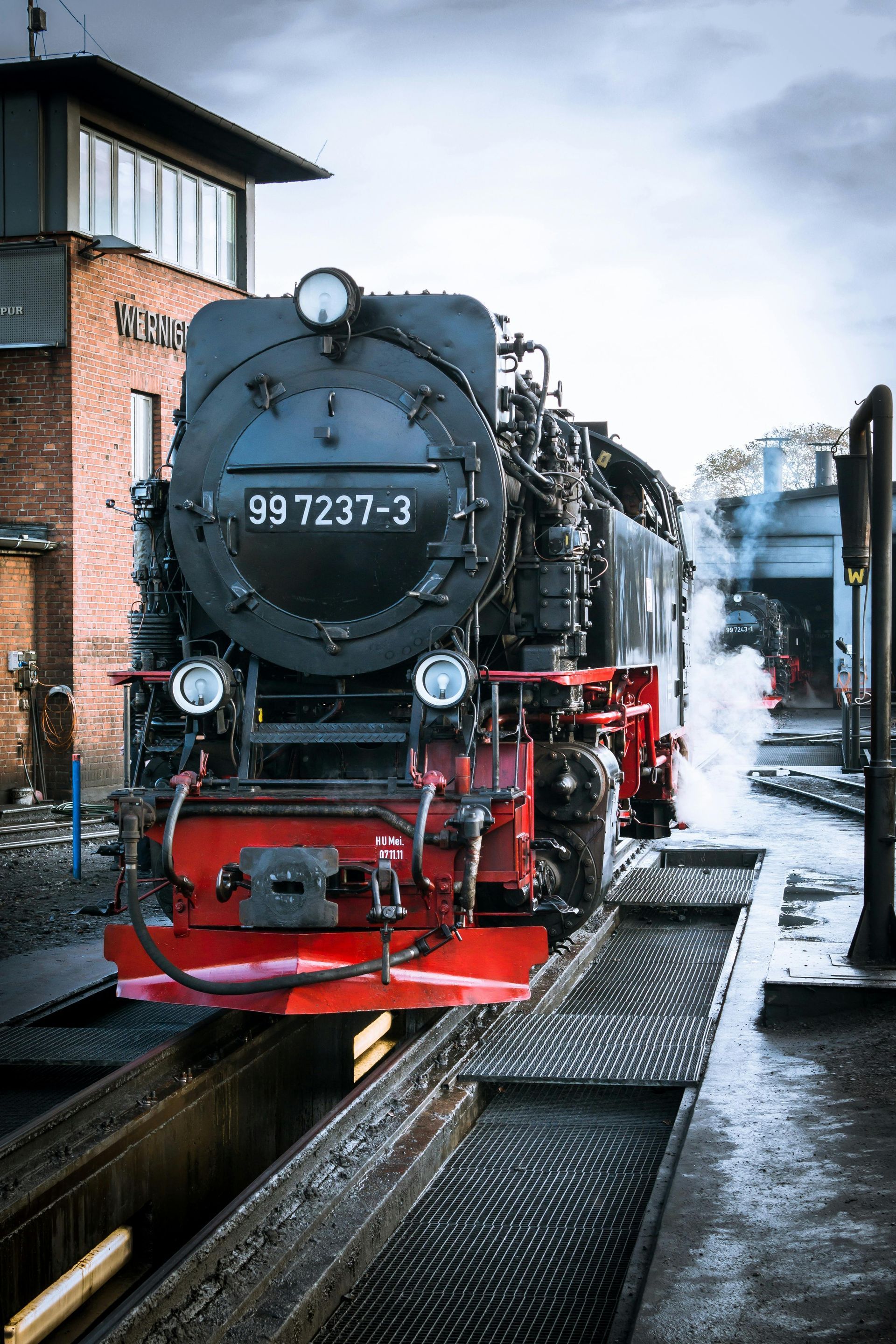Train on tracks at a train station with steam coming out the back of train