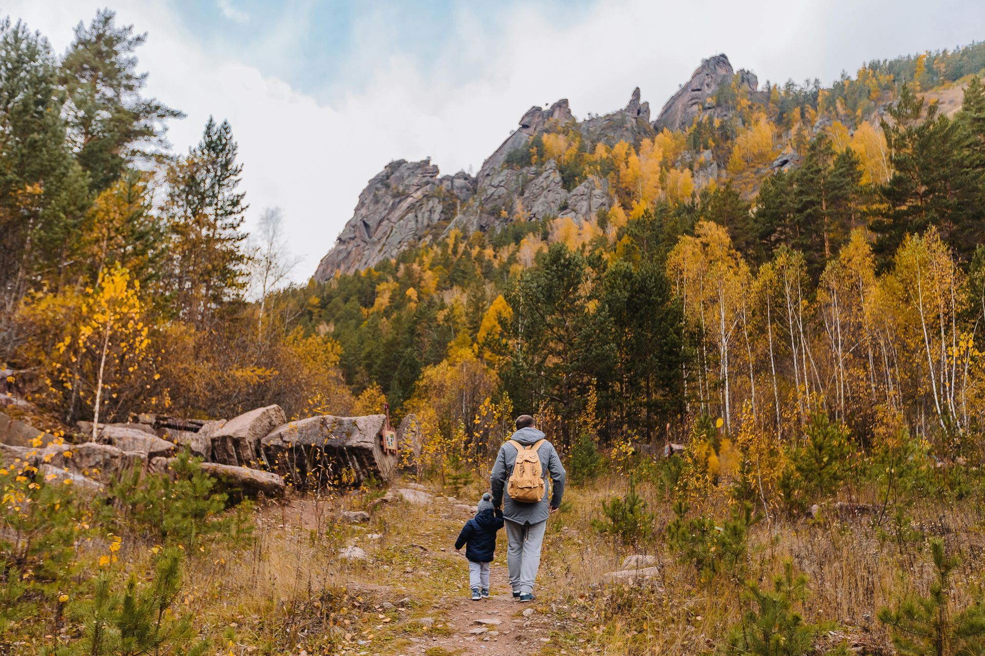 Person and child walking a trail outdoors, surrounding by fall leaves