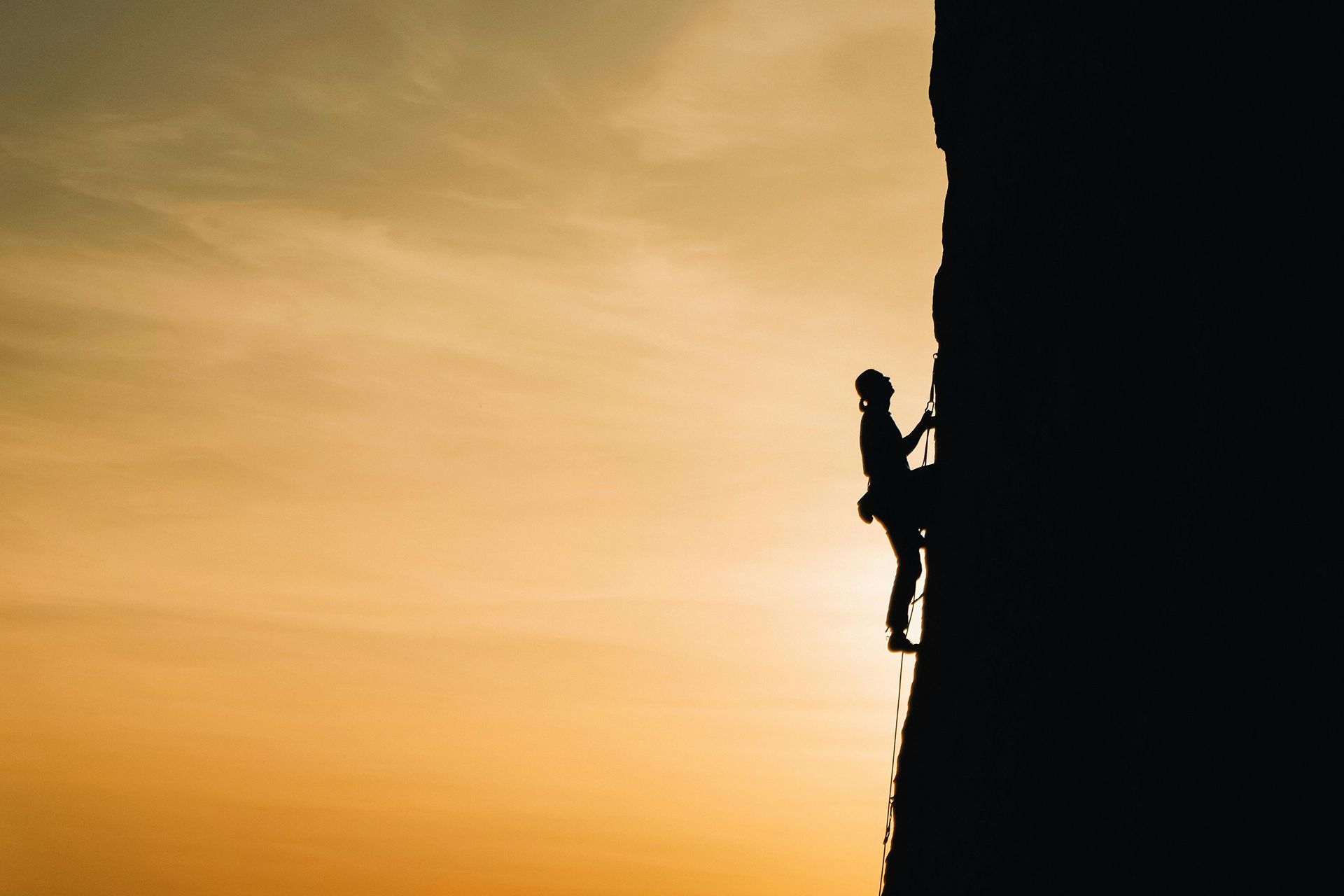 Man performing extreme vertical rock climbing during sunrise