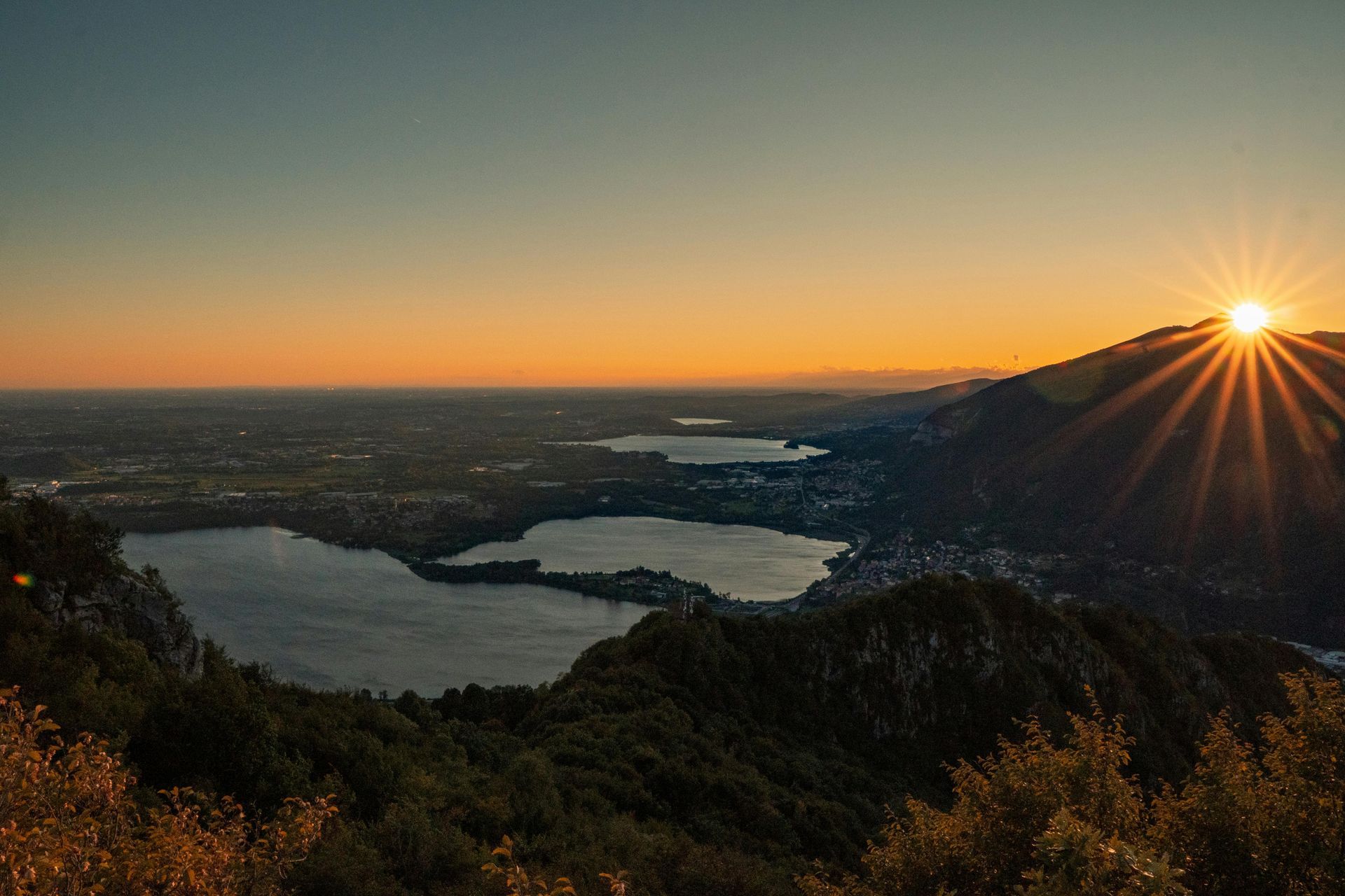Mountain view of multiple lakes with the sun setting behind grassy hill