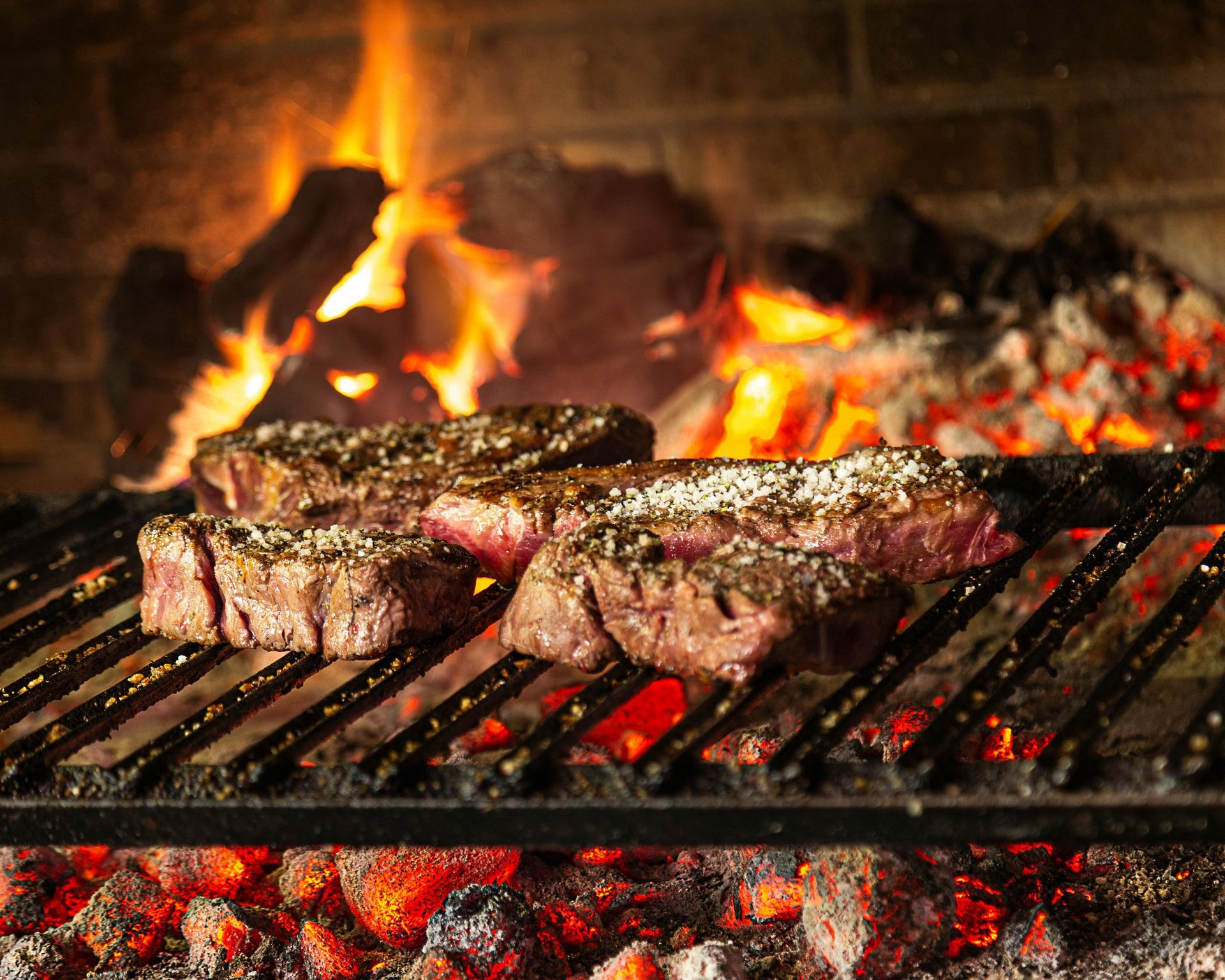 Steak being grilled on open flame with fire and logs in the background