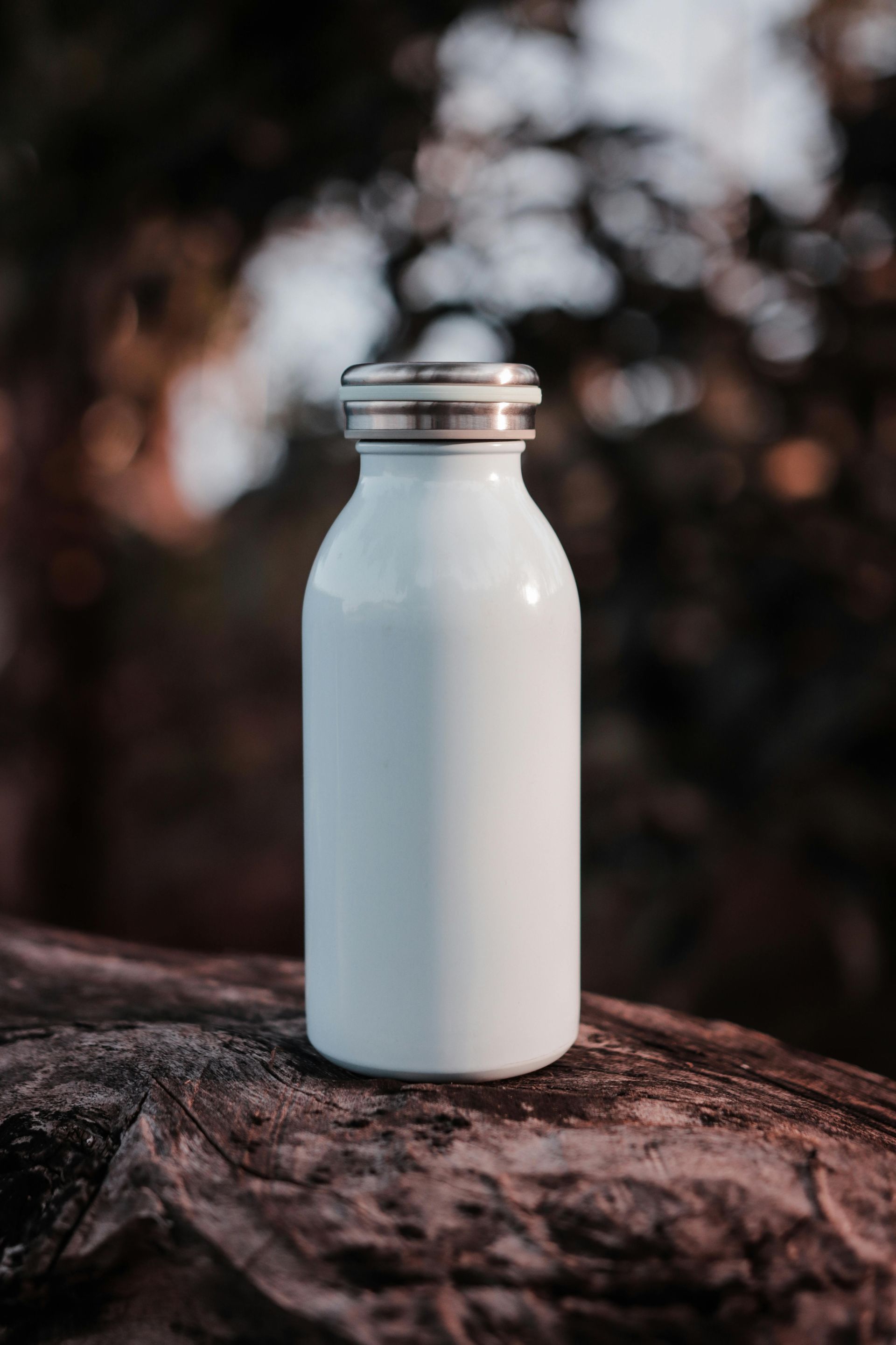 White water bottle sitting on log with blurred trees in the background