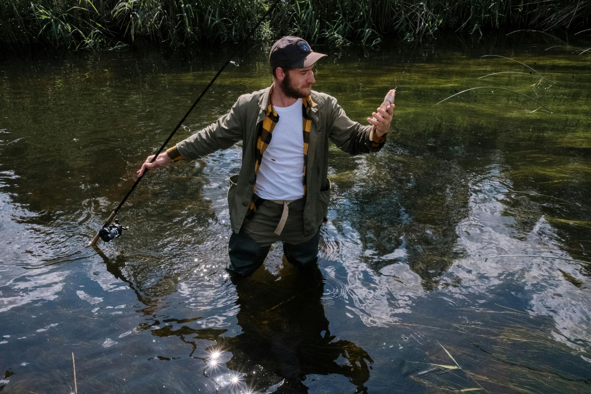 Man in layered clothing holding a fish and reel while standing in the river