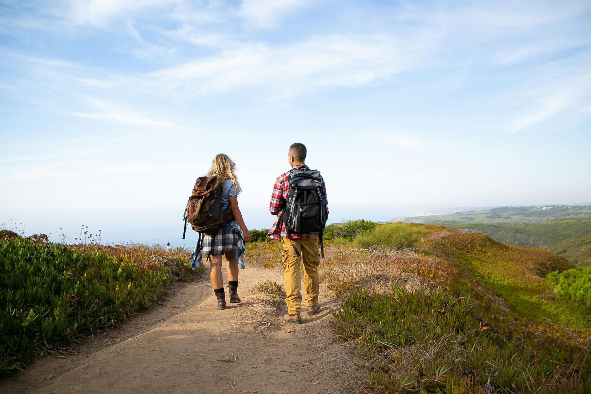Couple walking together down dirt trail with lush green grass and bright blue skies