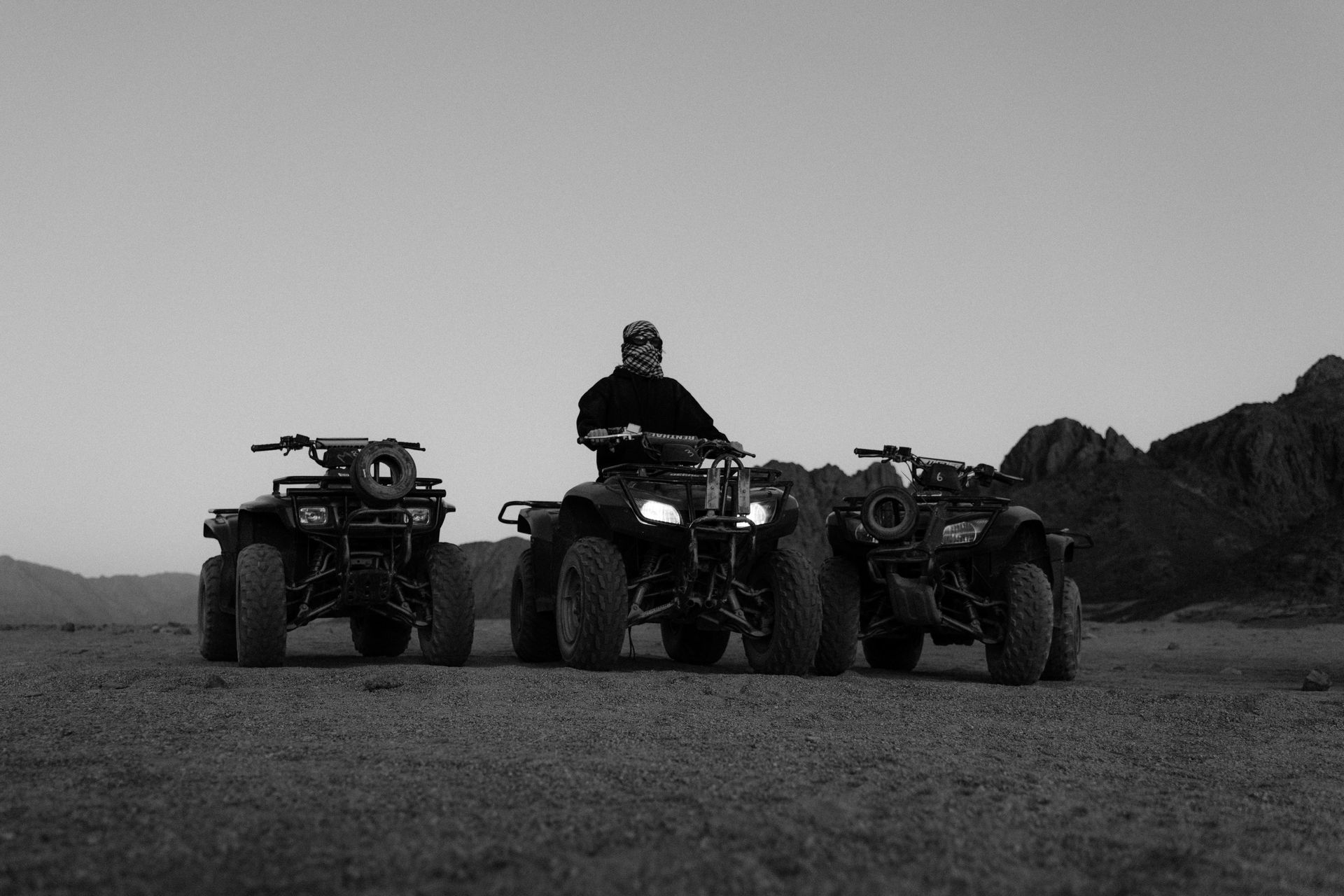 Person sitting on ATV in dirt field with surrounding ATVs 
