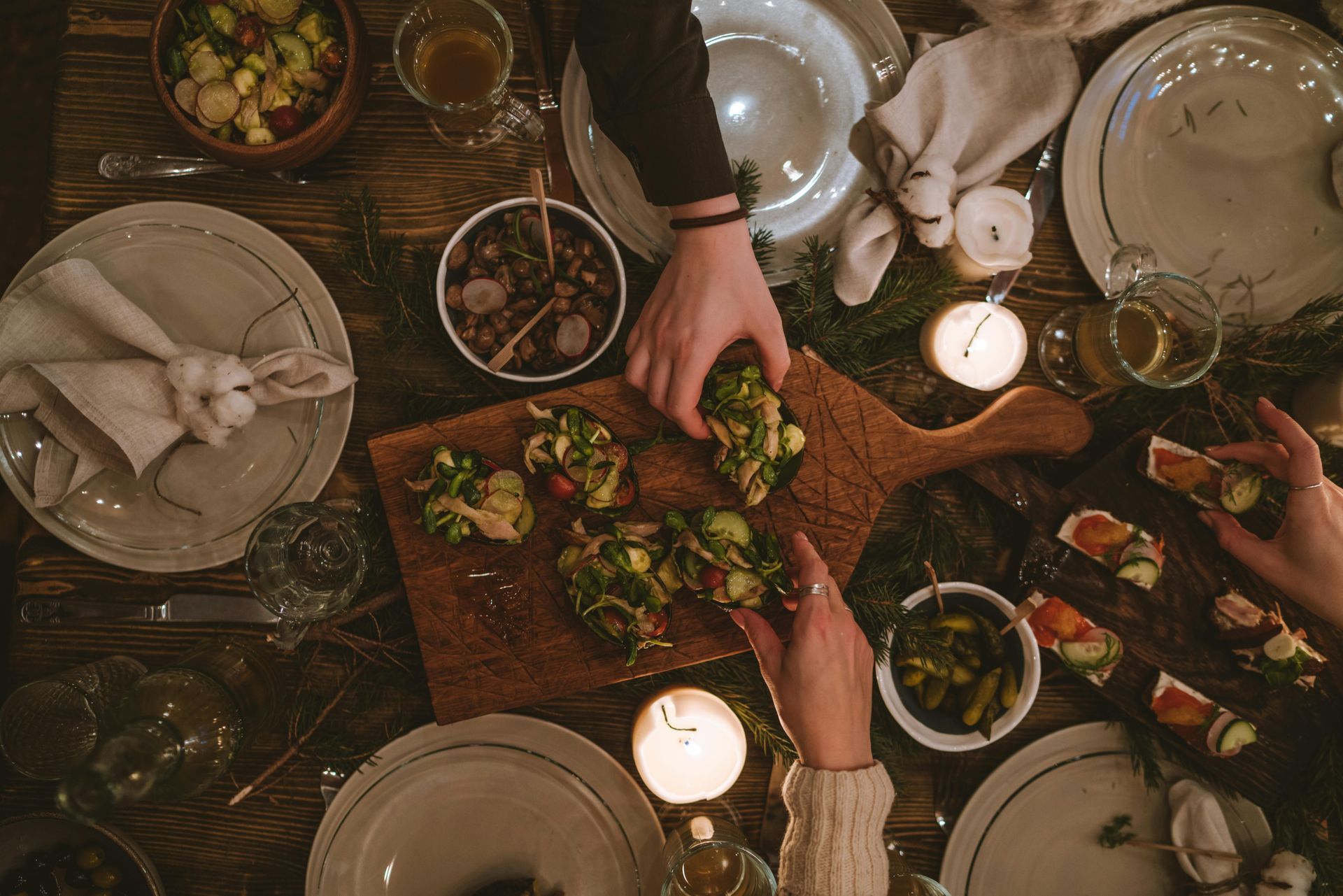People reaching for food at a candlelit dinner table. Food on a wooden board with side dishes