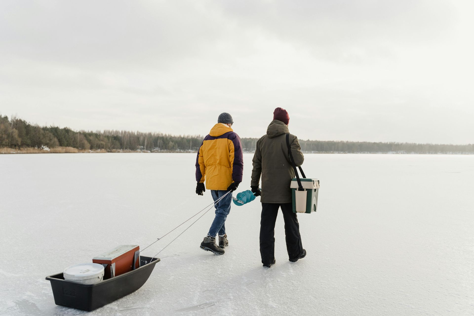Two people walking on ice, pulling a sled with fishing gear on a hazy day