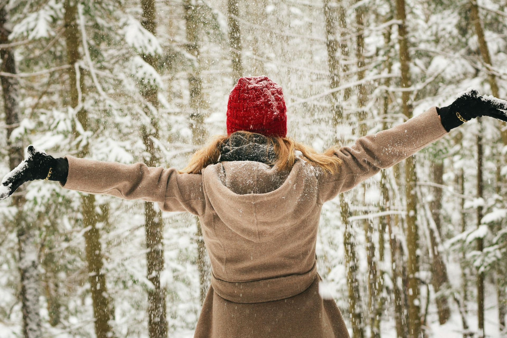 Woman in red hat and coat with arms outstretched in snowy forest