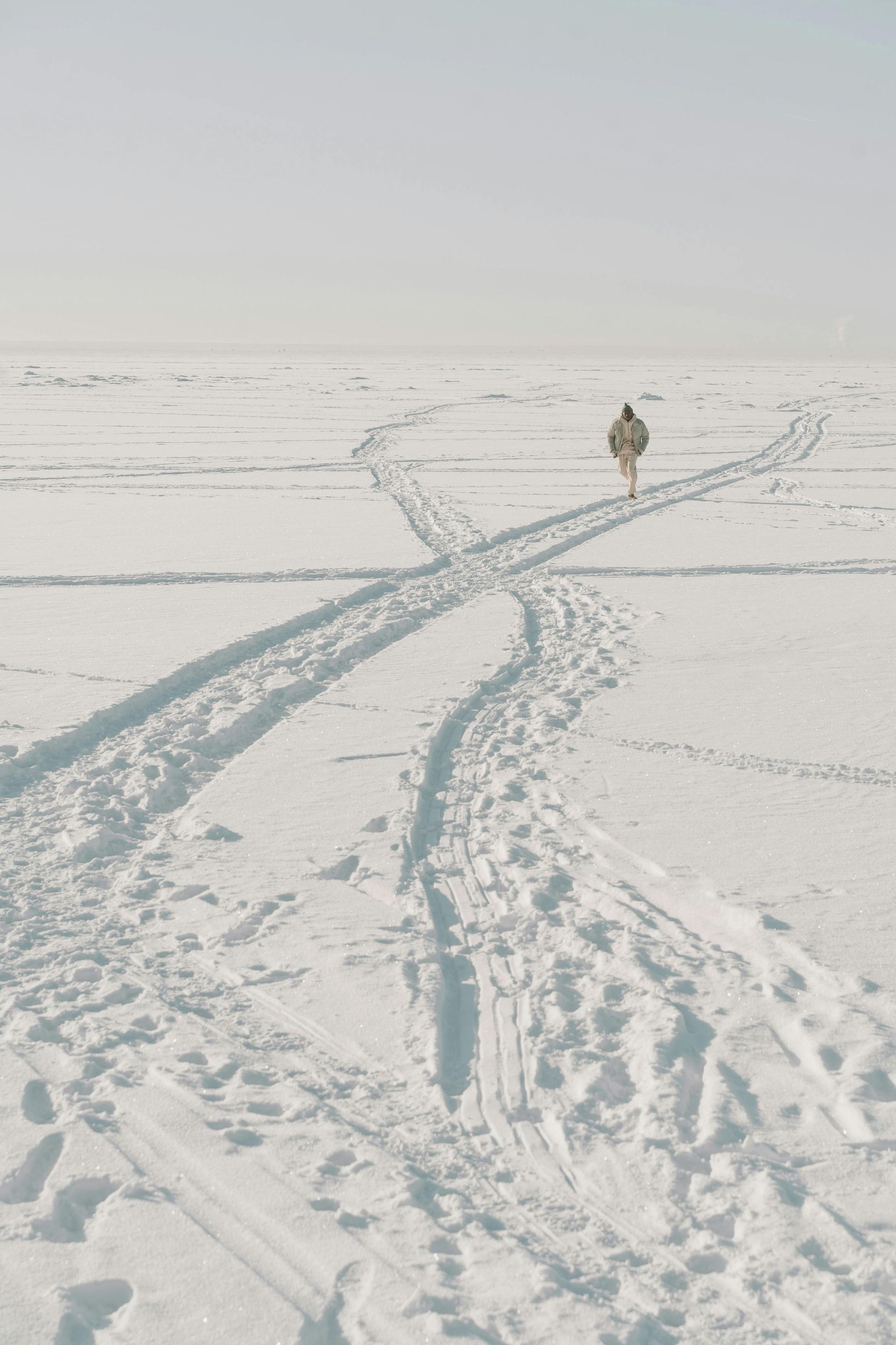 A person snowshoeing through a snowy set of tracks on an open field