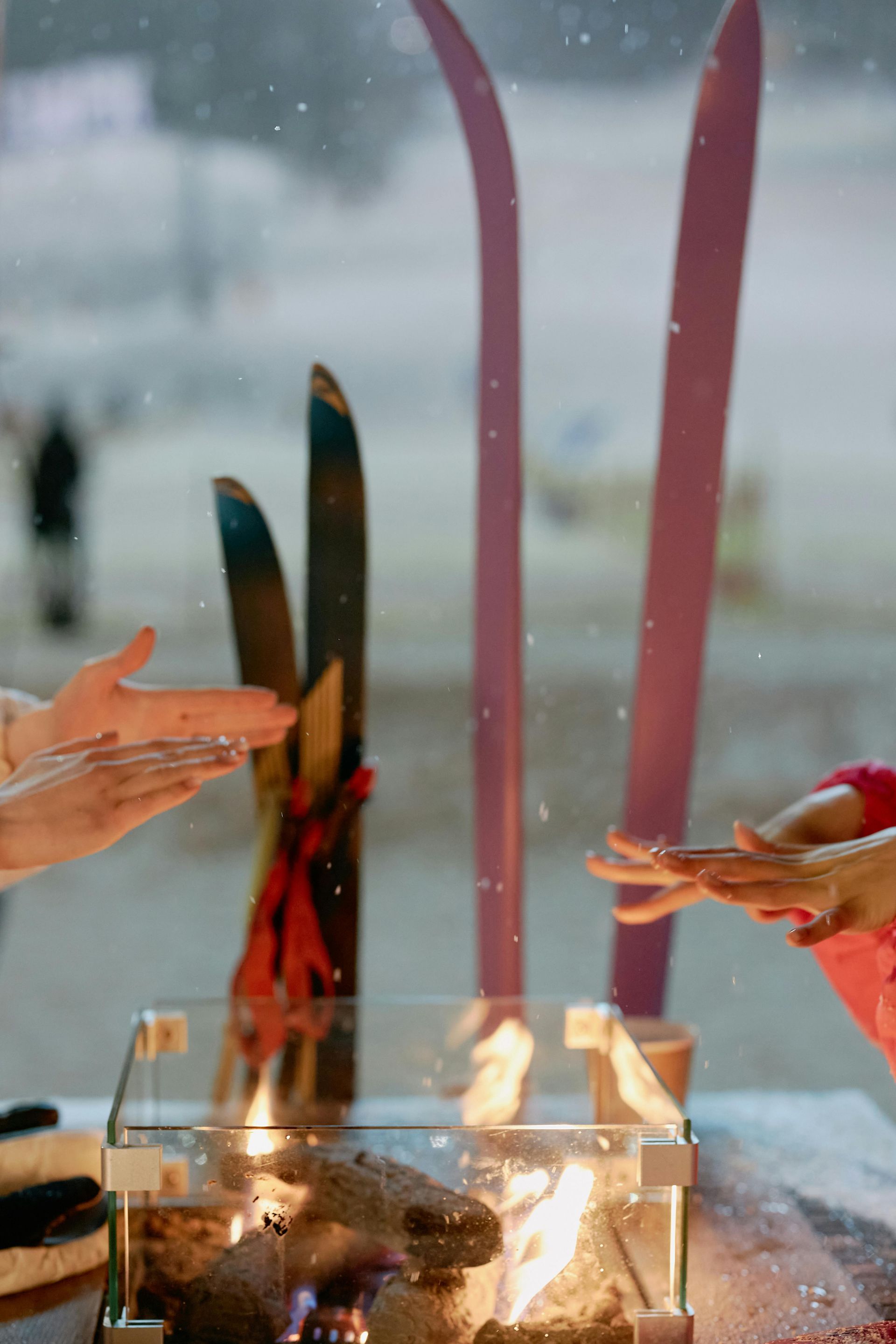 People warming their hands over outdoor firepit with skis nearby