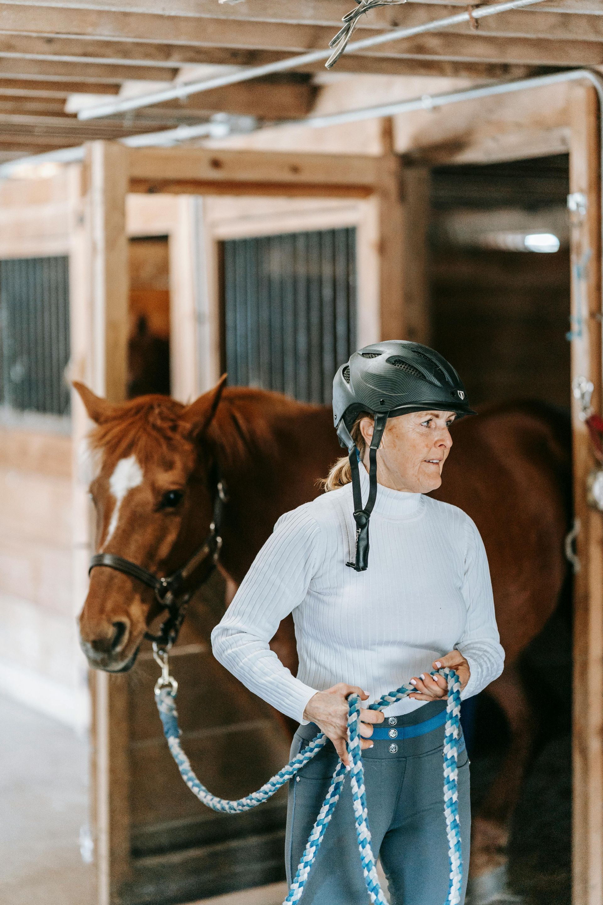 Woman wearing safety helmet, leading a horse out of stables