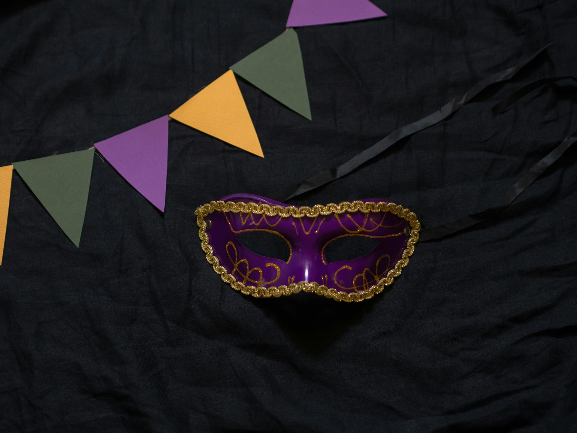 A purple and gold Mardi Gras mask resting on black fabric