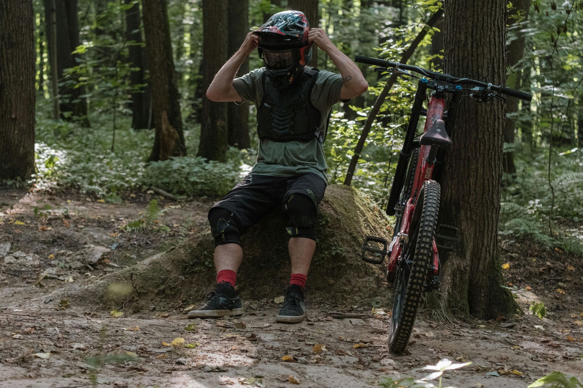 Person resting on rock after biking, with bike sitting against tree in the woods