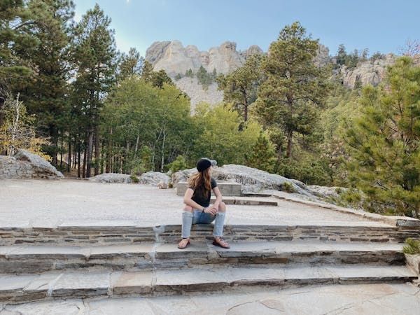 Woman sitting on sets with trees and Mount Rushmore in the background with blue skies