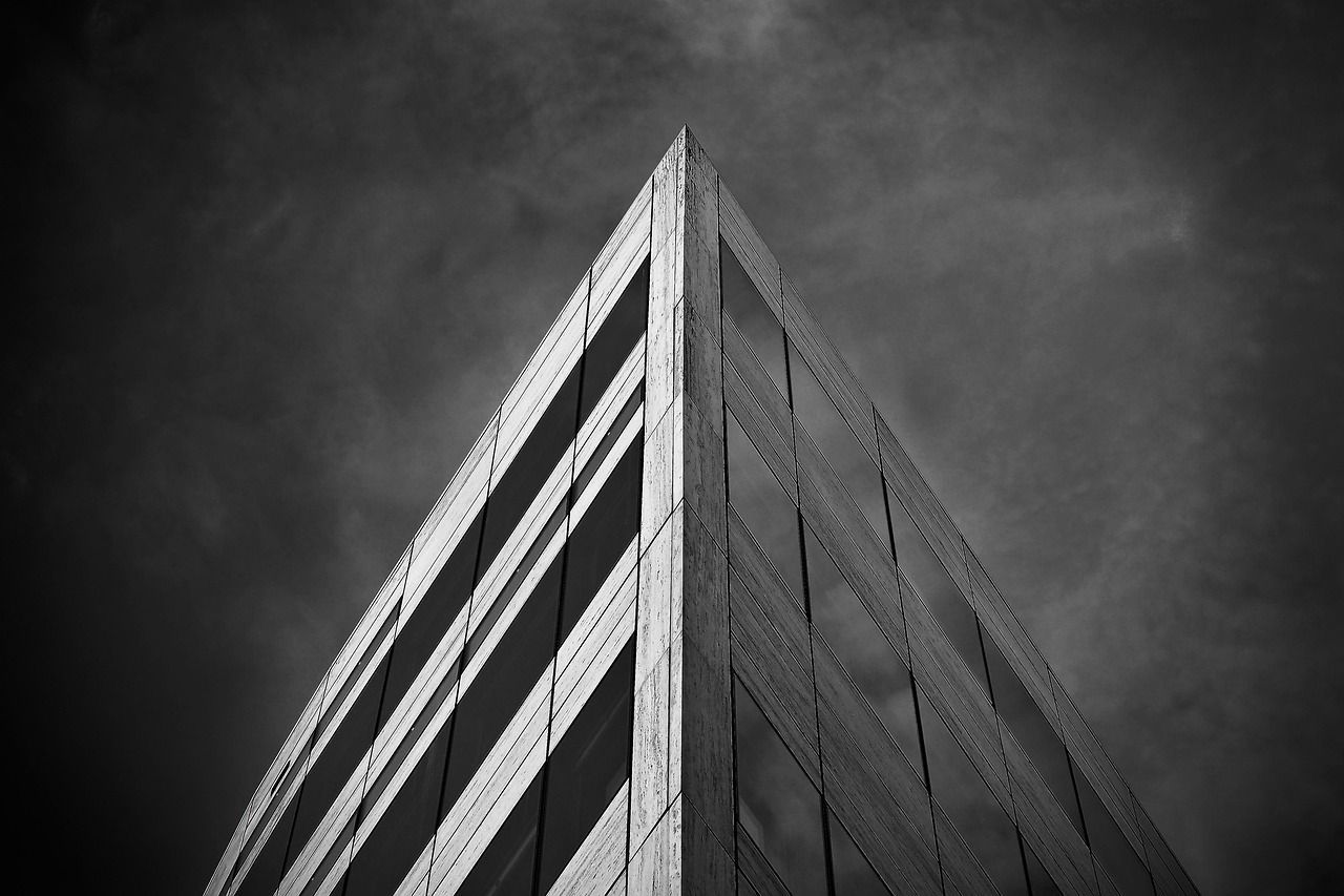 A black and white photo of a tall building against a cloudy sky.