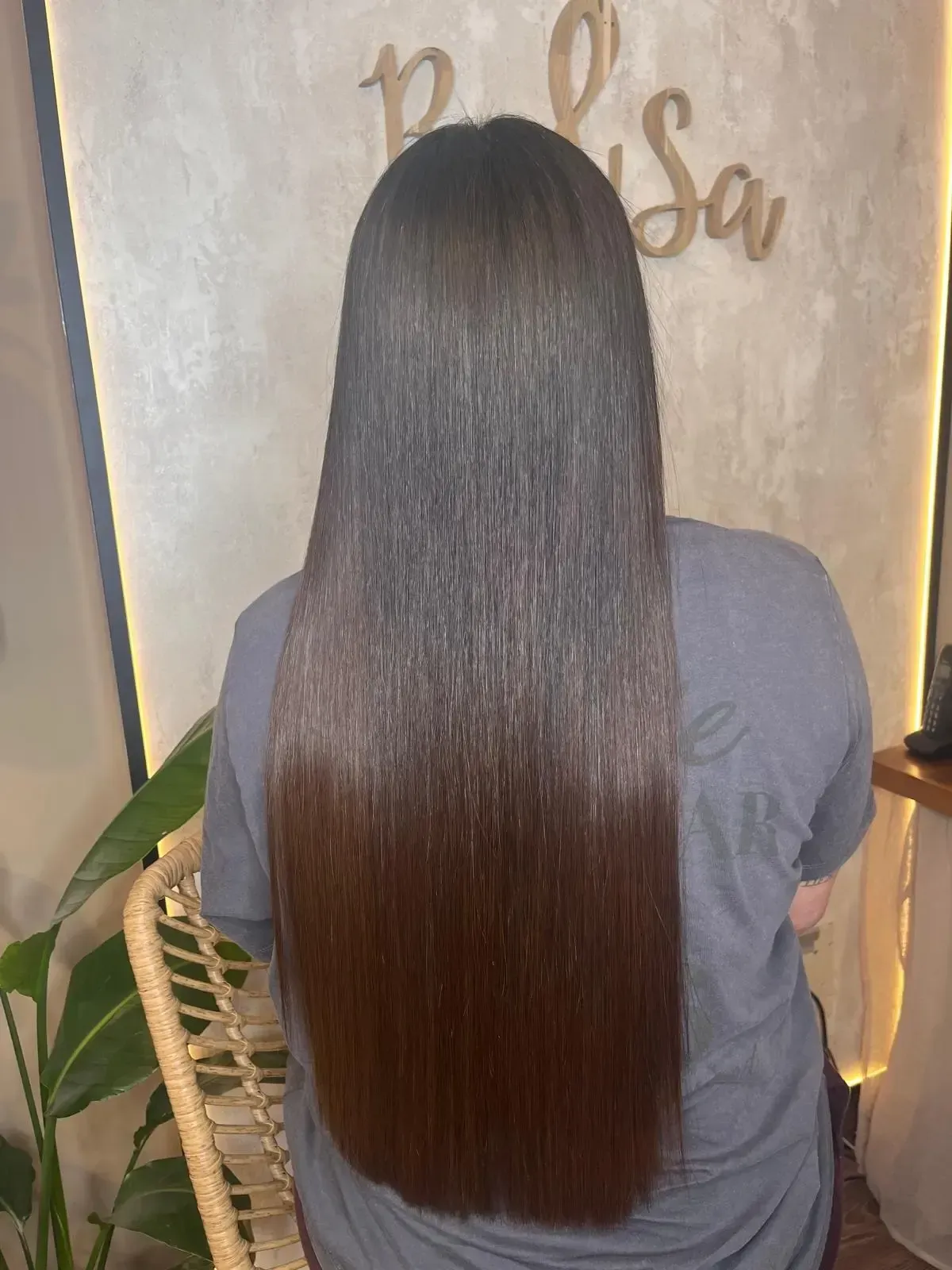 Las manos de una estilista aplicando extensiones de cabello individuales con microanillas al cabello castaño ondulado y con mechas de una clienta.