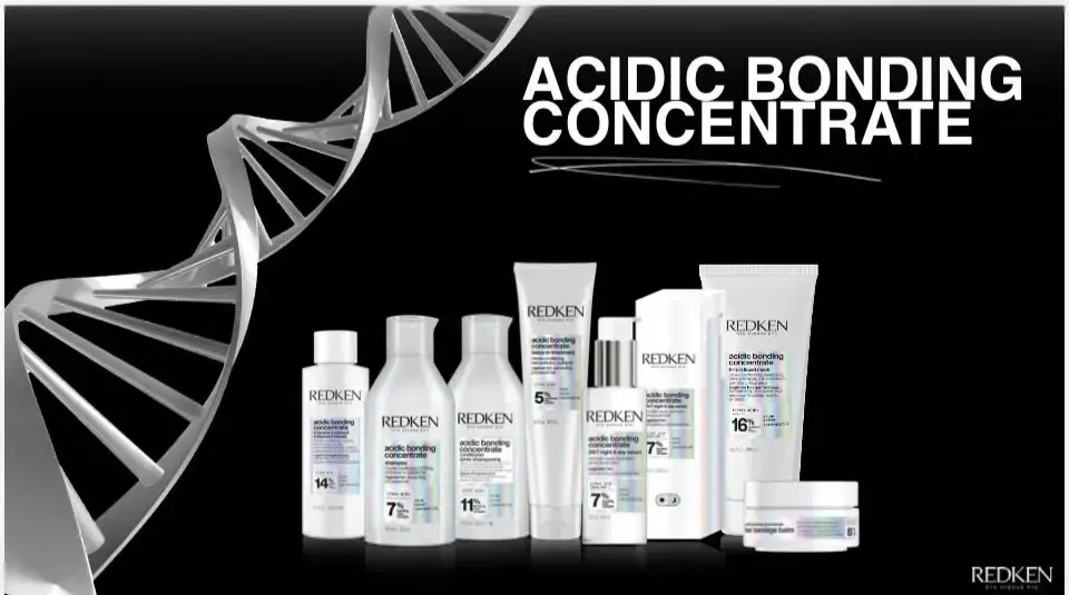 Una persona con cabello largo, ondulado y castaño está sentada en una silla de peluquería mientras un estilista le sujeta un mechón de cabello.