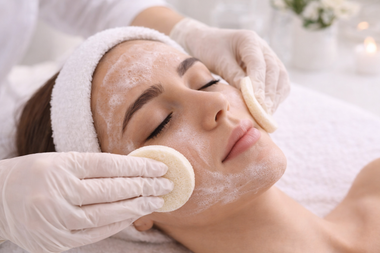 Una persona recibe un relajante lavado de cabello en un salón de belleza, con espuma jabonosa en la cabeza y productos tipo spa sobre una mesa de madera.