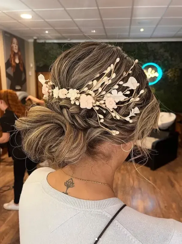 Una persona con cabello largo, ondulado y castaño con reflejos color miel, que lleva un suéter verde, dentro de una peluquería.