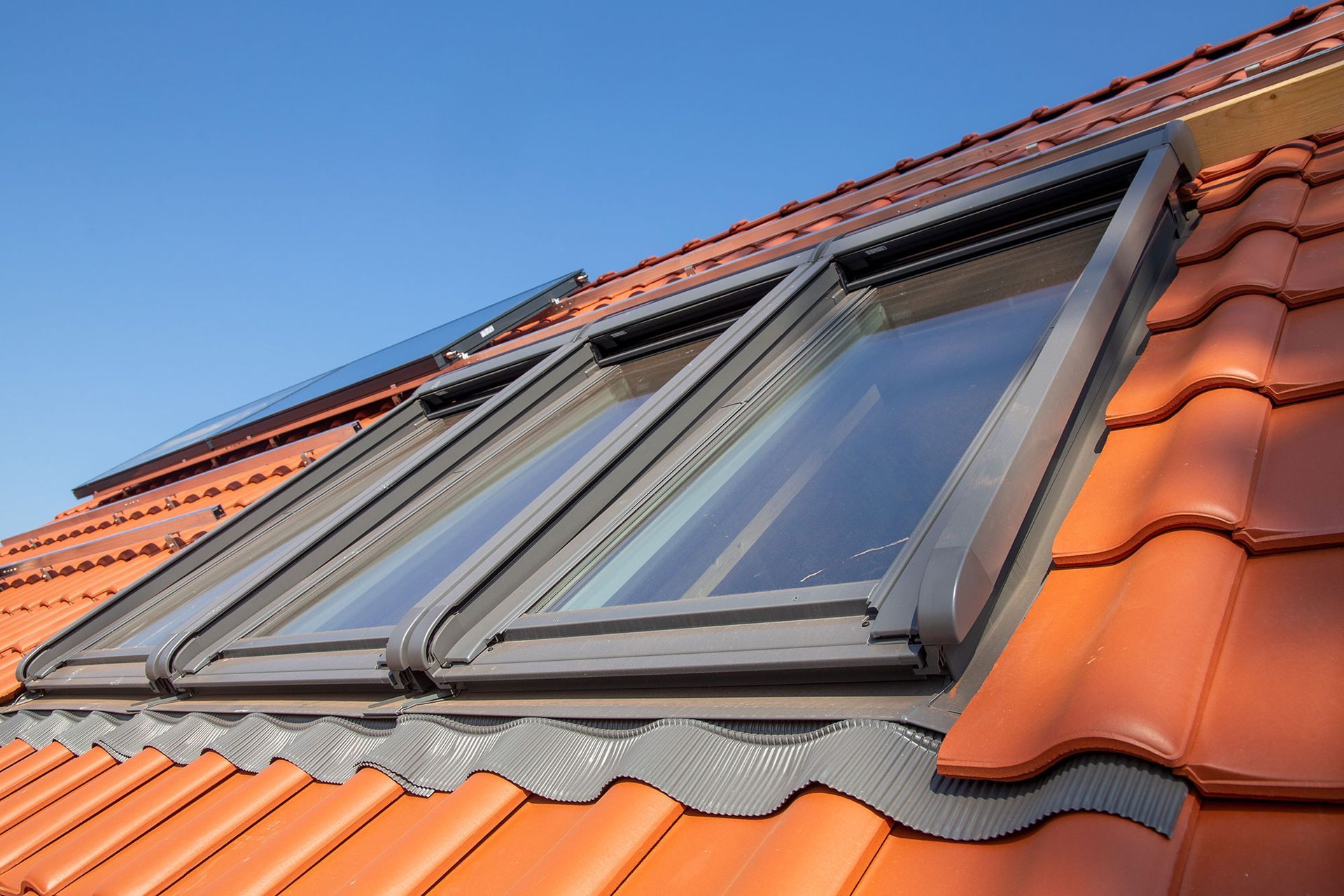 Dachfenster, eingefasst in orangefarbene Terrakotta-Dachziegel unter blauem Himmel