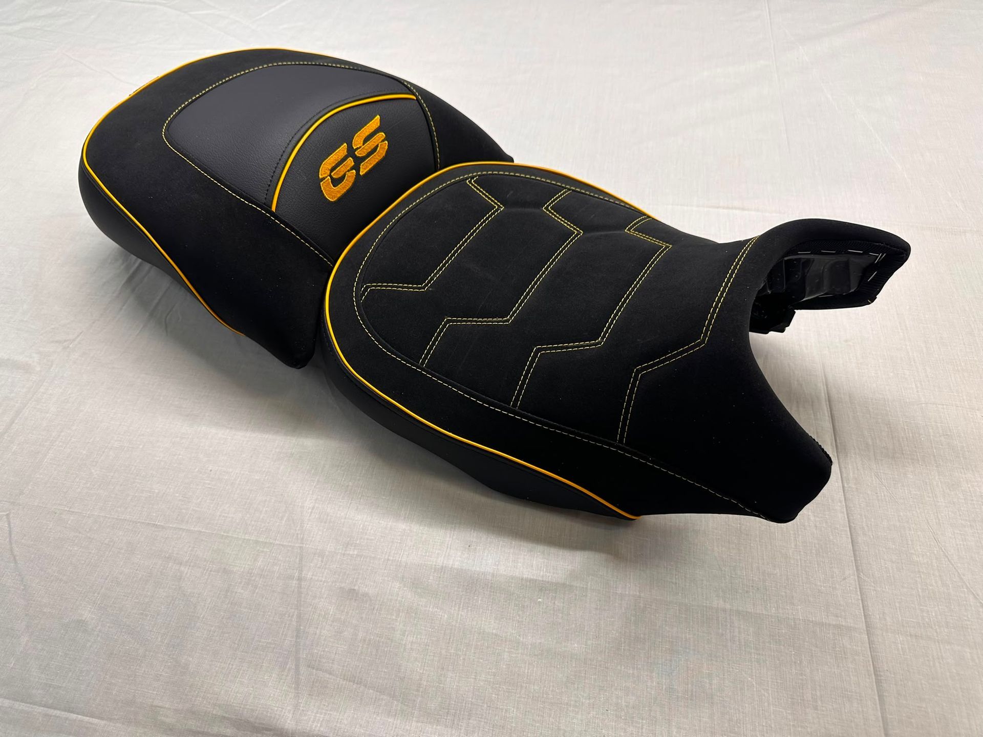 Funda negra para asiento de motocicleta con costuras amarillas y el número 55 sobre una superficie blanca