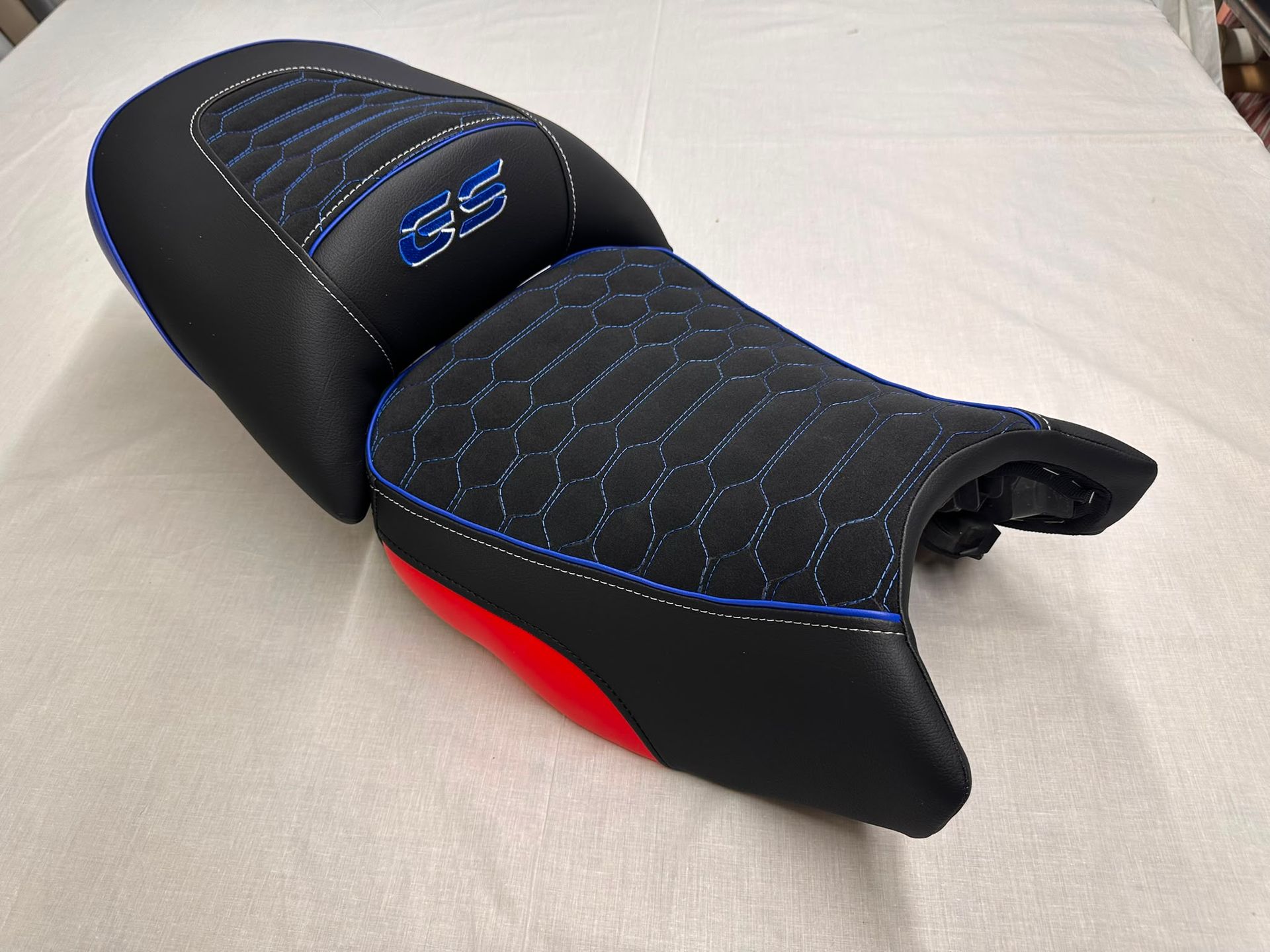 Asiento de moto negro y azul con la parte inferior roja sobre una superficie clara