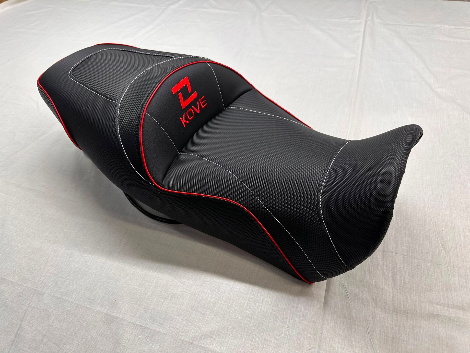 Asiento de motocicleta negro y rojo con funda texturizada sobre un fondo claro