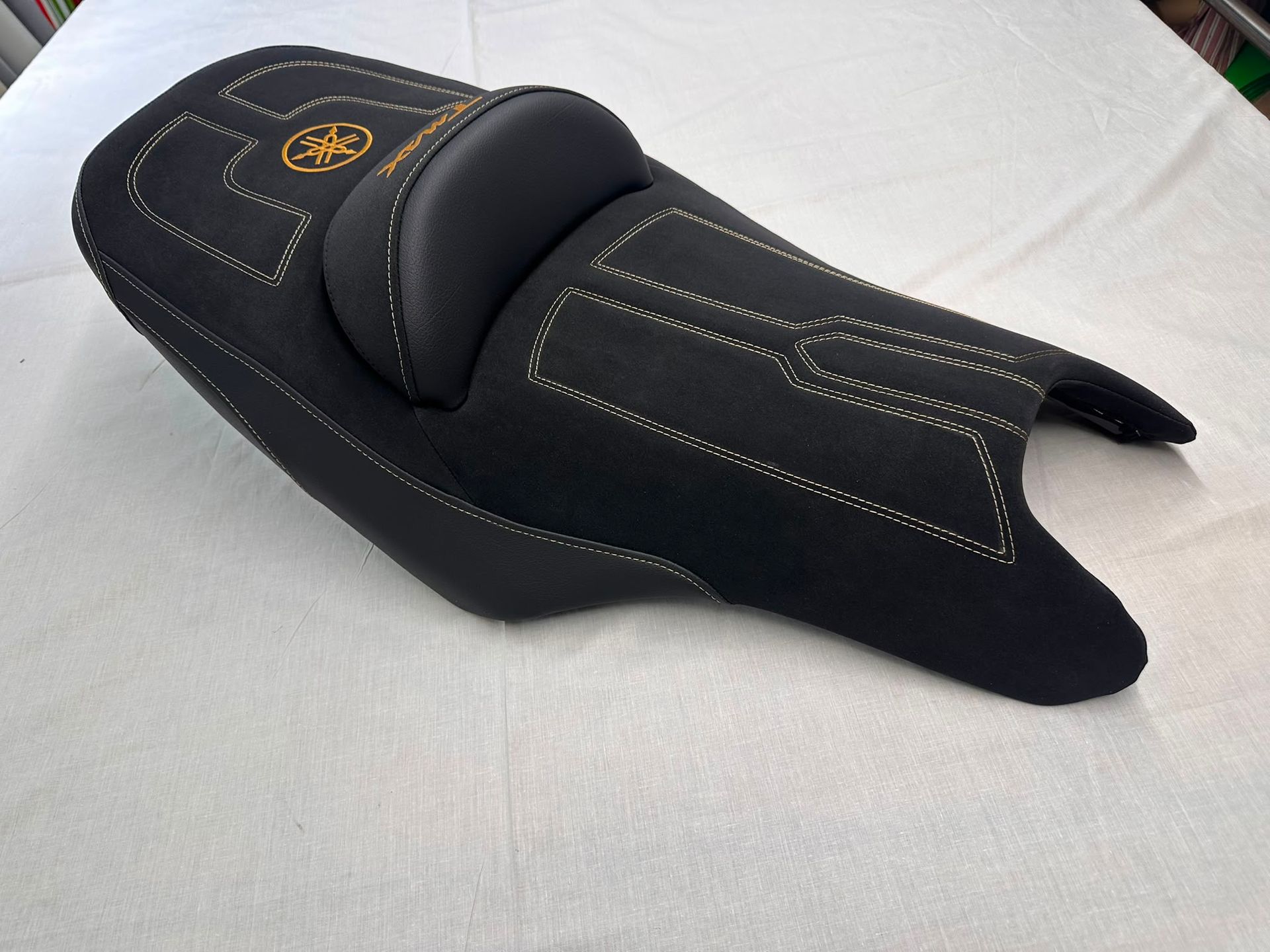 Funda de asiento de moto negra acolchada con pespuntes amarillos sobre fondo blanco