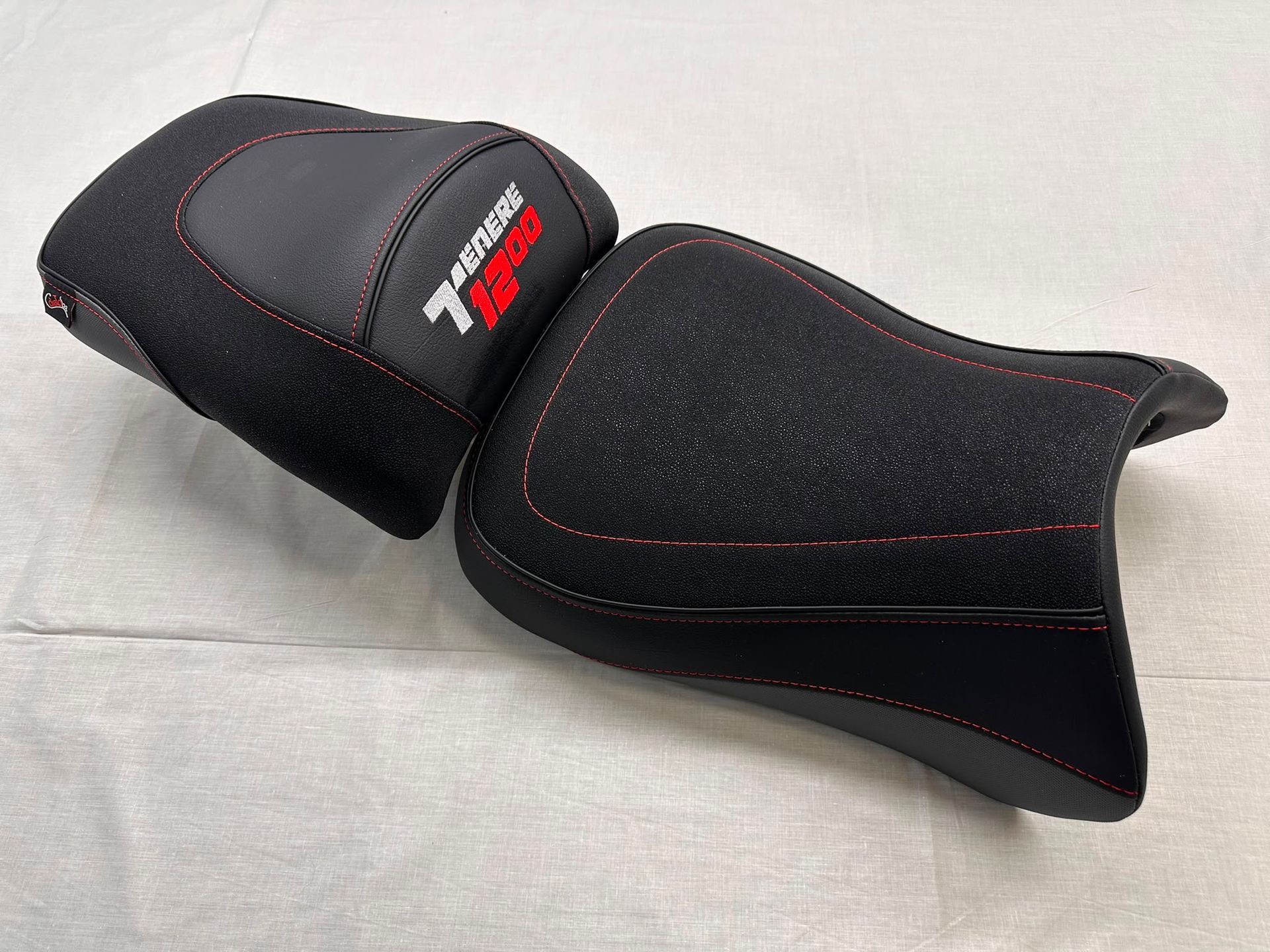 Funda de asiento para motocicleta negra y gris, con costuras rojas, sobre un fondo claro