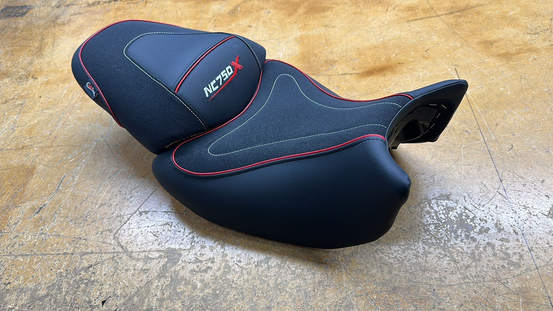 Asiento negro de motocicleta con costuras rojas sobre un suelo de hormigón