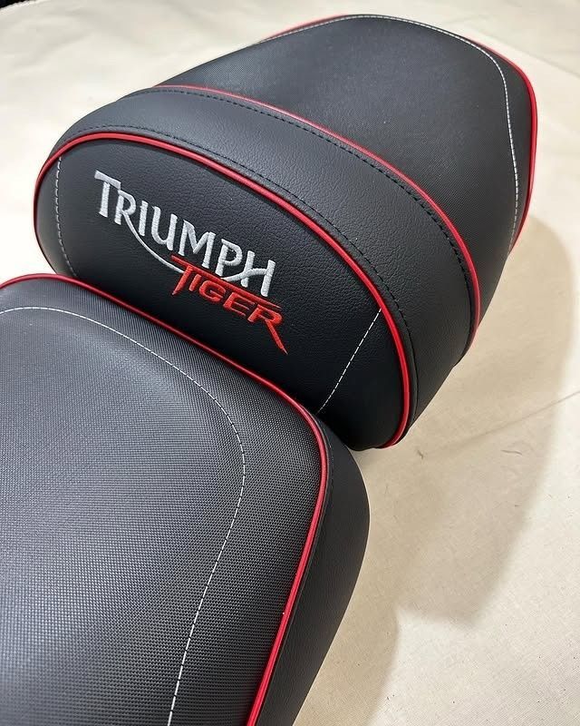 Un juego de asientos de motocicleta Triumph Tiger de color negro con ribetes rojos y detalles de costuras blancas.