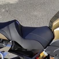Vista lateral del asiento doble ergonómico negro de una motocicleta, con paneles de tela texturizada y costuras detalladas.