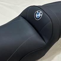Un asiento de motocicleta negro con costuras blancas y un logotipo circular de BMW en la sección del respaldo.