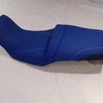Un asiento de motocicleta de color azul brillante, contorneado, con costuras distintivas y un diseño de dos niveles sobre un fondo blanco.