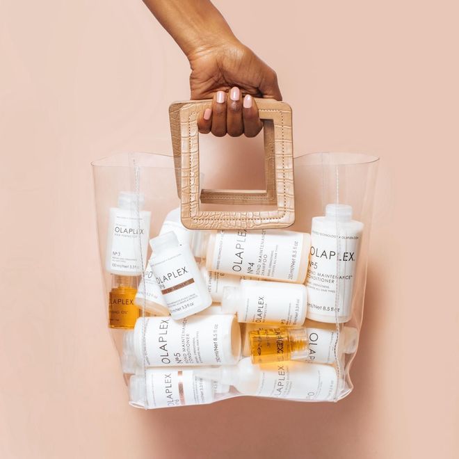 Una persona sostiene una bolsa transparente llena de botellas de productos para el cabello.
