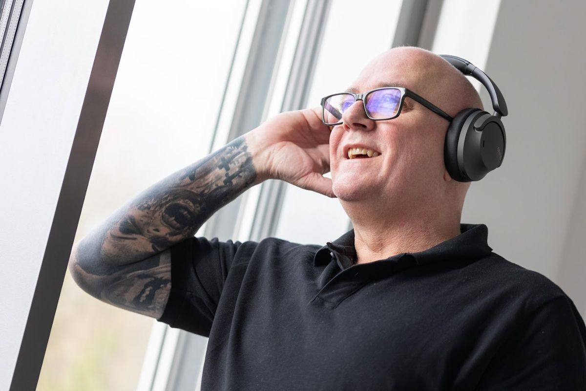 Ein Mann mit Kopfhörern und Brille steht vor einem Fenster.