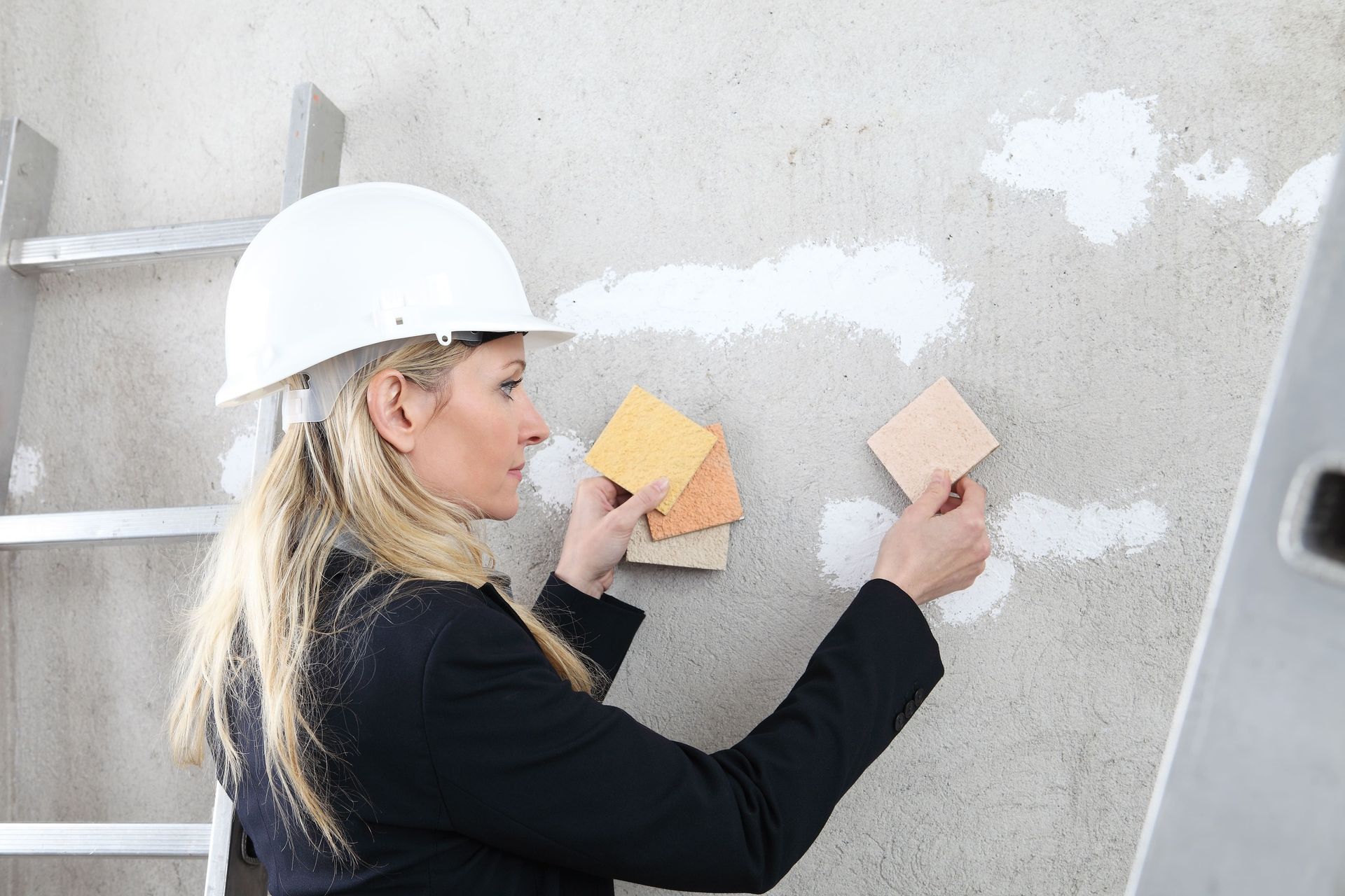 Una mujer que lleva un casco mira muestras de pintura en una pared.