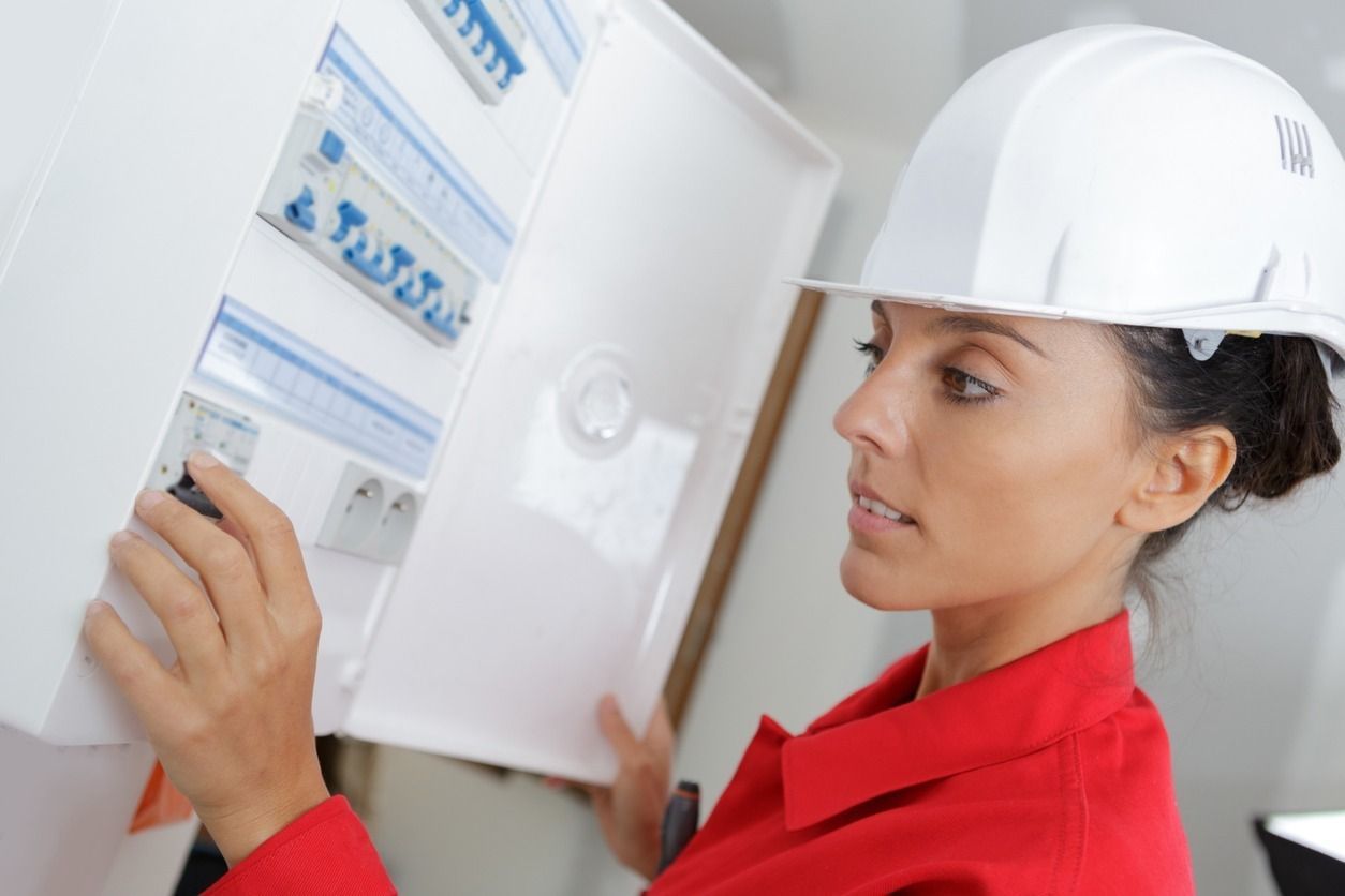 Una mujer que lleva un casco está trabajando en una caja eléctrica.