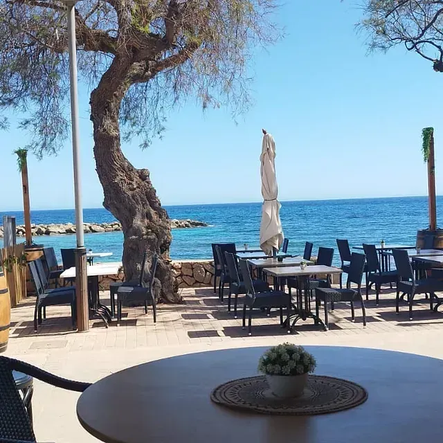 Una mesa con un jarrón de flores delante de mesas y sillas con vistas al océano.