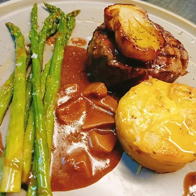 Un plato de comida con espárragos y salsa encima.