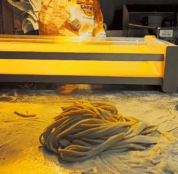 Una pila de fideos está sobre una mesa al lado de una bolsa de harina.