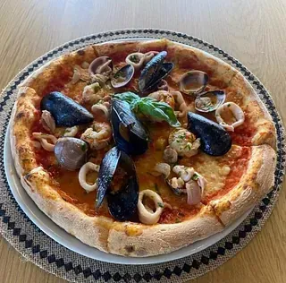 Una pizza con mariscos está en un plato sobre una mesa.