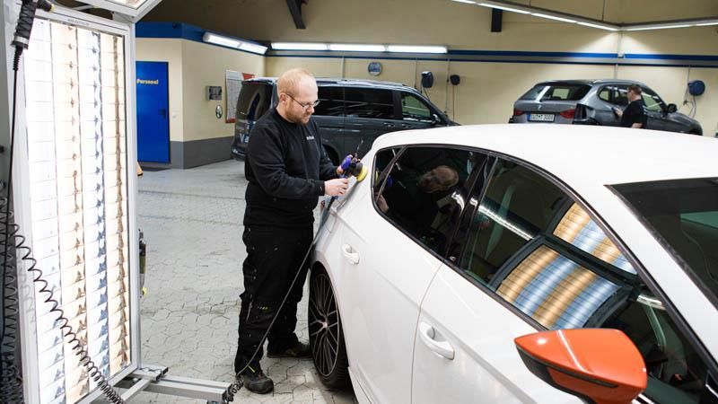 Ein Mann arbeitet in einer Garage an einem weißen Auto.